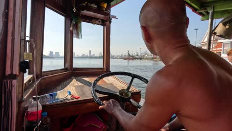 man steering boat with city skyline in background