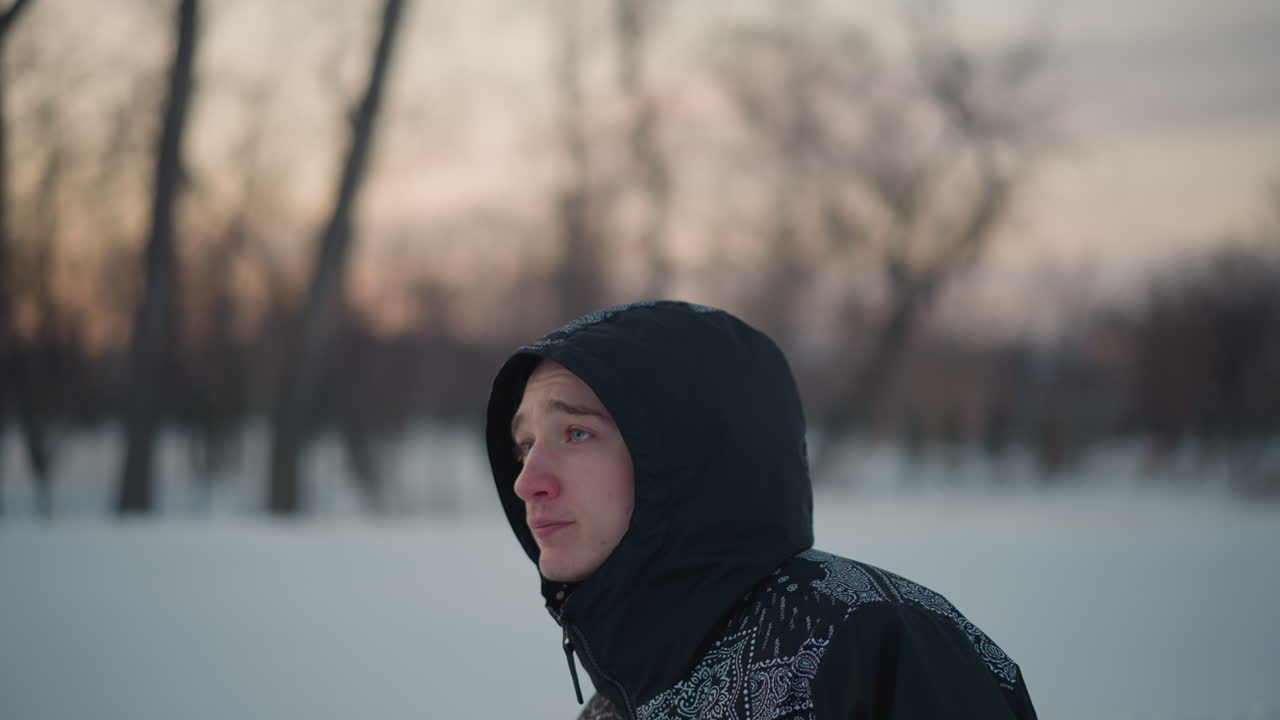 close up of white man in hoodie gliding on ice under soft winter sunset light with blur background of bare trees and park, visible breath mist rising, focused side profile, serene calm expression