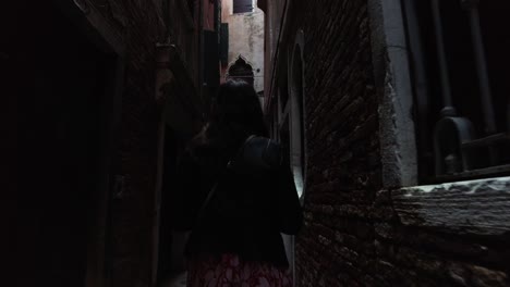 back view of a female vacationist walking on narrow streets in venice, italy