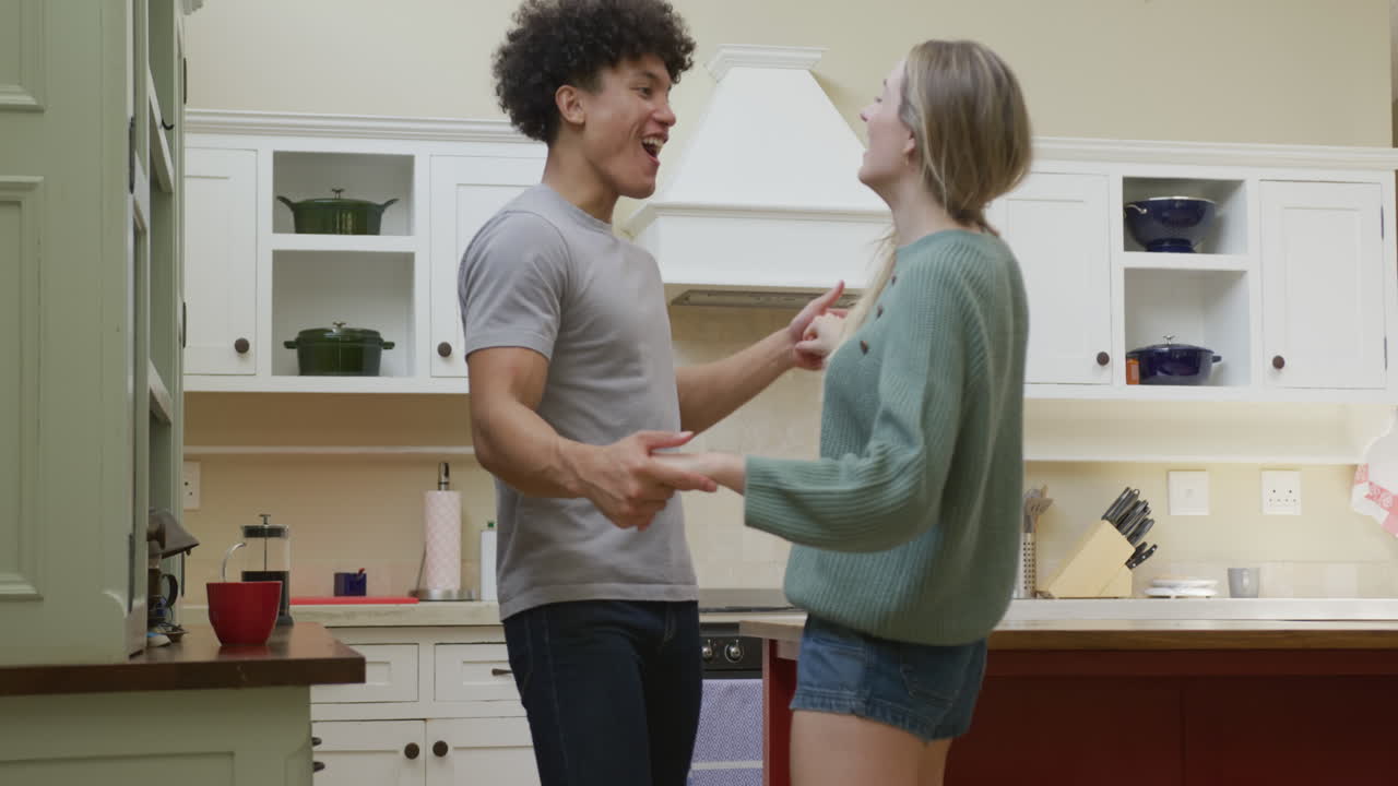 una pareja feliz de diferentes orígenes tomándose de la mano y bailando en casa