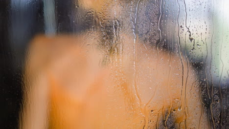 woman takes shower behind water drops flowing down on glass