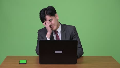 young handsome asian businessman working with laptop against green background