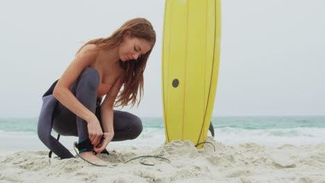 Side-view-of-Caucasian-female-surfer-tying-surfboard-leash-on-her-leg-surfboard-at-beach-4k