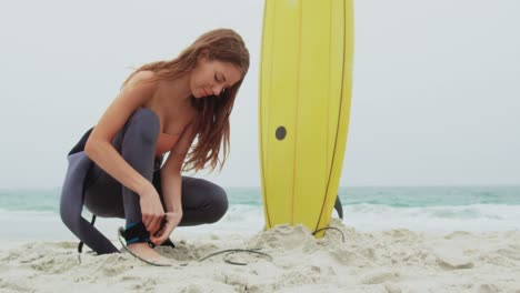 side view of caucasian female surfer tying surfboard leash on her leg surfboard at beach 4k