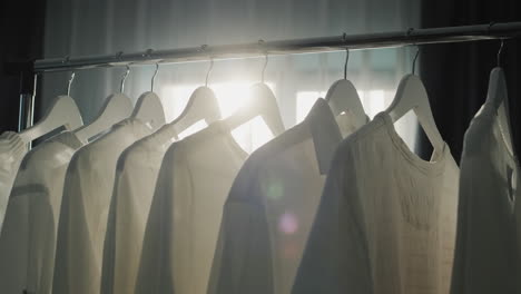 rack with hangers of white clothes in the rays of the sun from the window