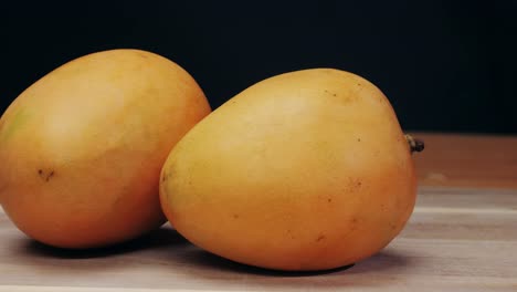two ripe mangoes on wooden surface