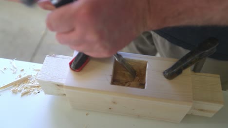 a woodworker uses a hand chisels and hammer to create a mortise for a piece of furniture