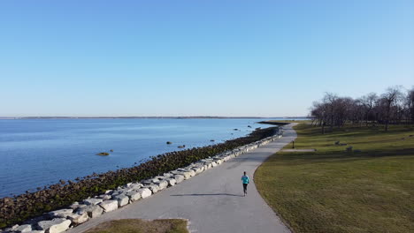 Excelente-Toma-Aérea-De-Una-Mujer-Corriendo-Por-El-Océano-En-Rhode-Island