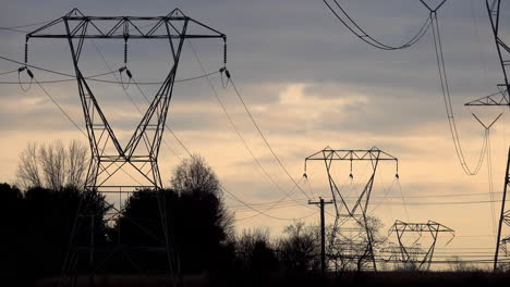 Electrical-transmission-towers-and-trees-with-somber-sky-at-sunset