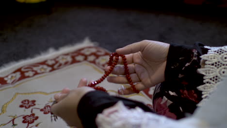 over the shoulder view of female hands holding red prayer beads sitting on prayer mat