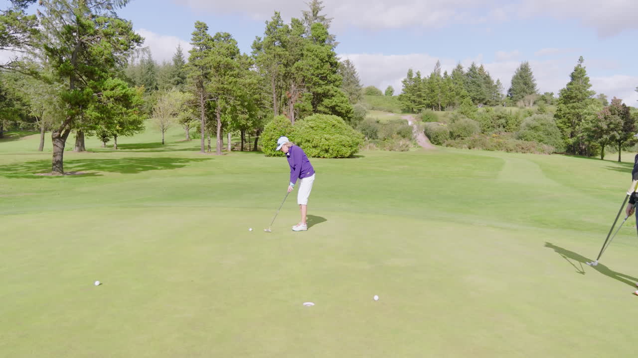 Female golf players playing golf and knocking golf ball into cup on golf course on cloudy day