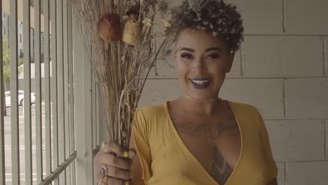 Beautiful-and-cheerful-girl-with-a-tattoo-and-a-modern-hairstyle-dancing-in-a-yellow-dress-with-a-dried-bouquet