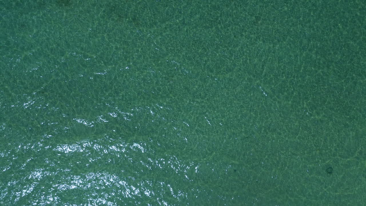 Aerial top down clear water in sea, low waves and empty background of coast