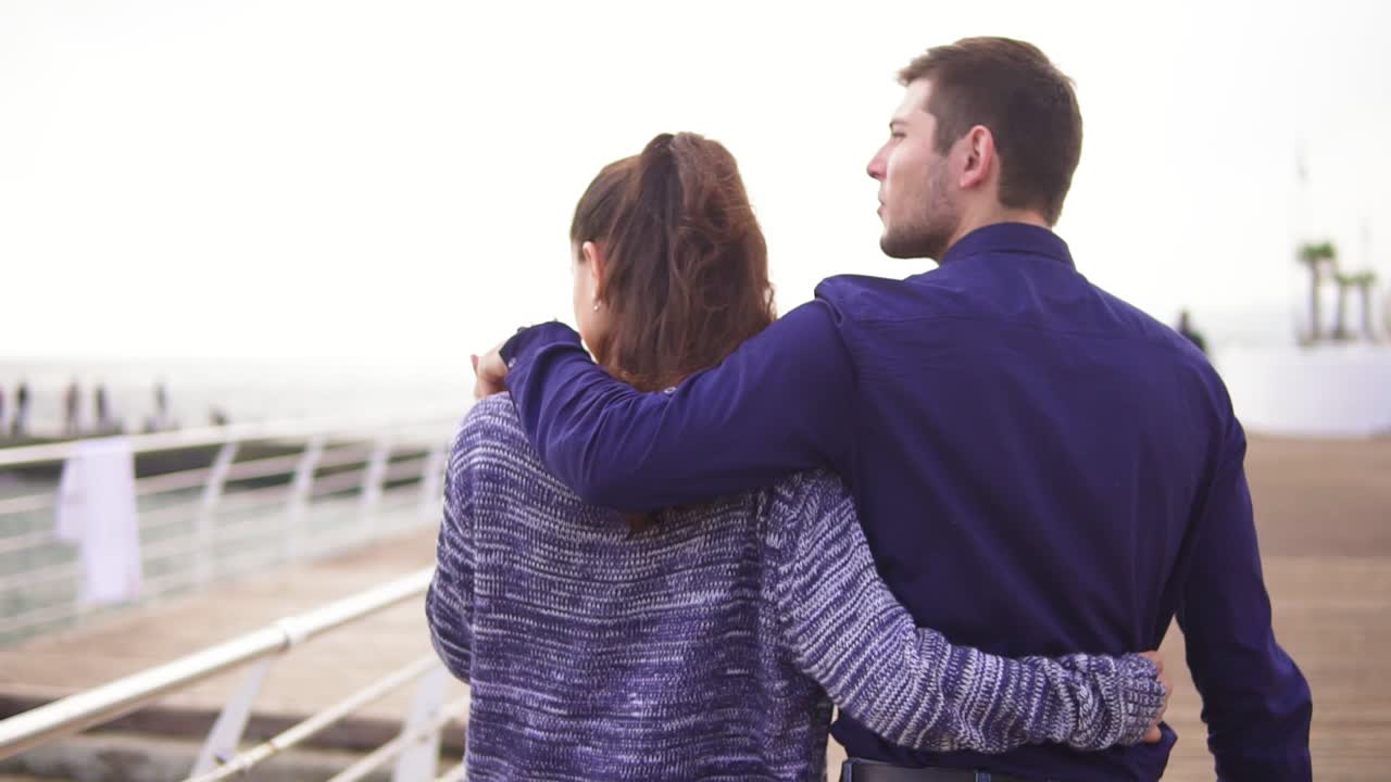 Close-up back view of young beautiful couple walking in the street embracing each other and kissing. Romantic date during the