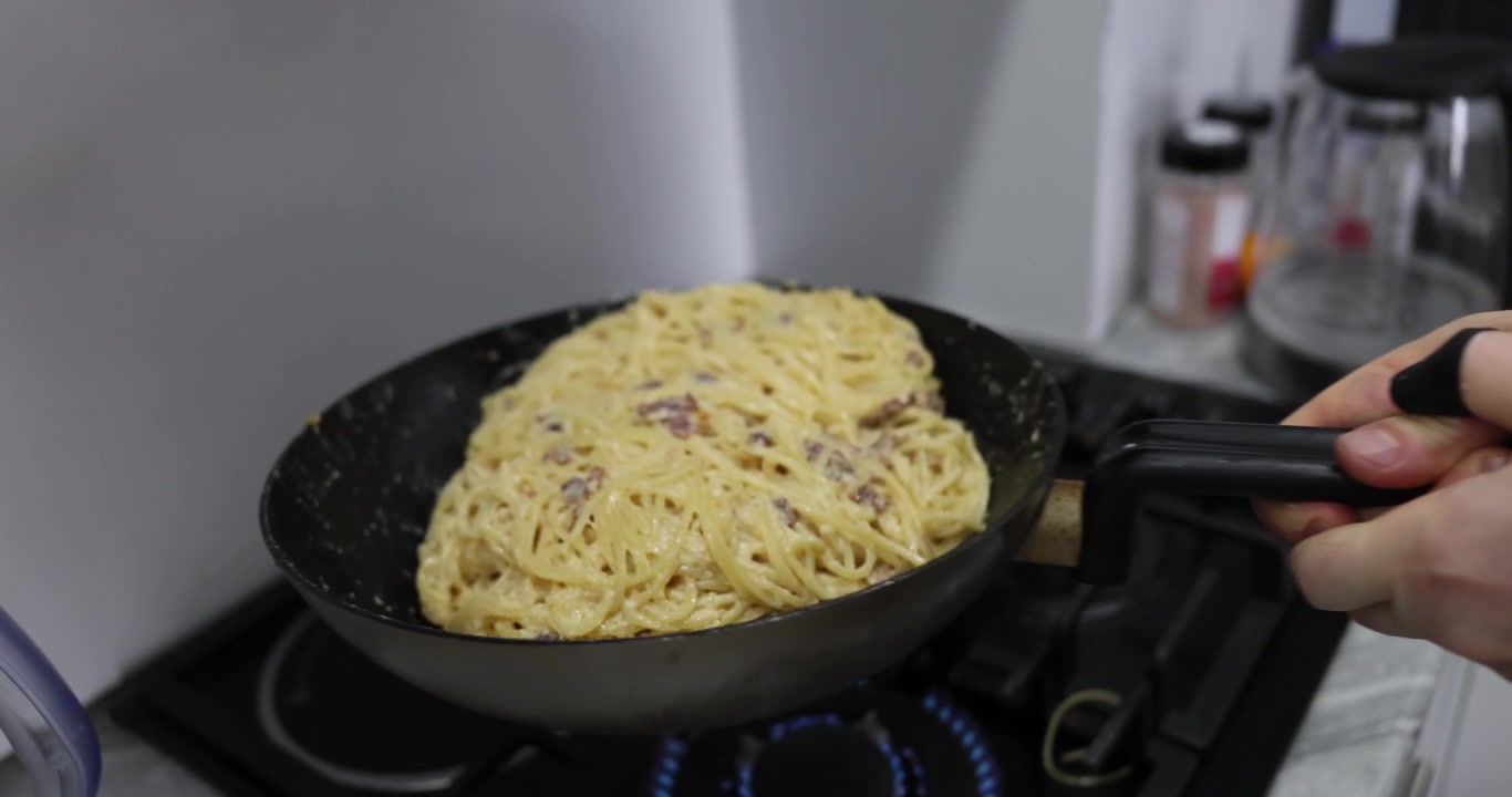 Il cuoco mescola spaghetti saporiti con pancetta croccante e salsa cremosa.