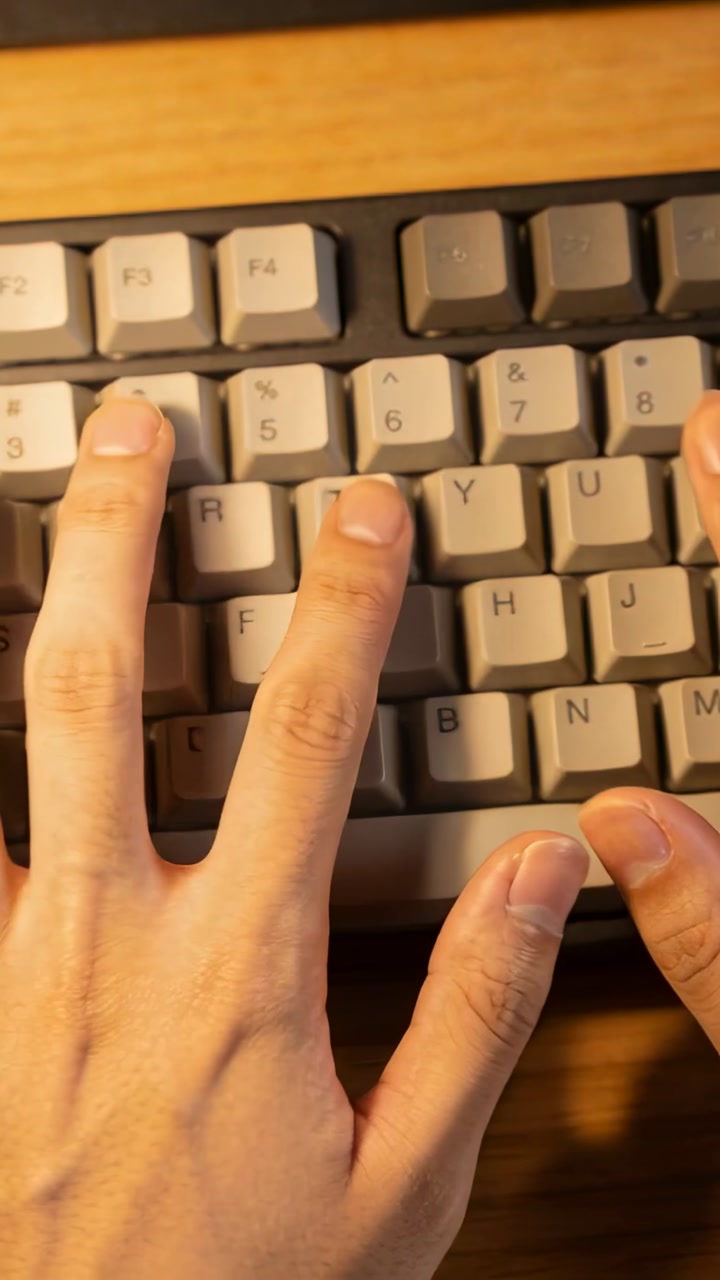Vertical video: Entering frame, adult hands hovering, pressing keys to type at desk, beige keyboard