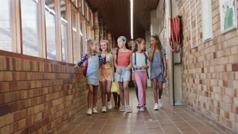 happy diverse schoolgirls with school bags walking in corridor at elementary school