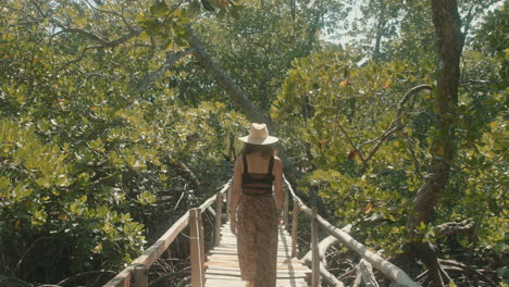 Zeitlupe-Von-Hinten-Einer-Attraktiven-Kaukasischen-Frau-Mit-Strohhut,-Die-Eine-Holzbrücke-In-Einem-Grünen-Wald-überquert