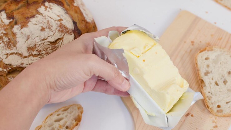 Top-down view of hands arranging crusty sourdough bread and unwrapping fresh butter on white background.