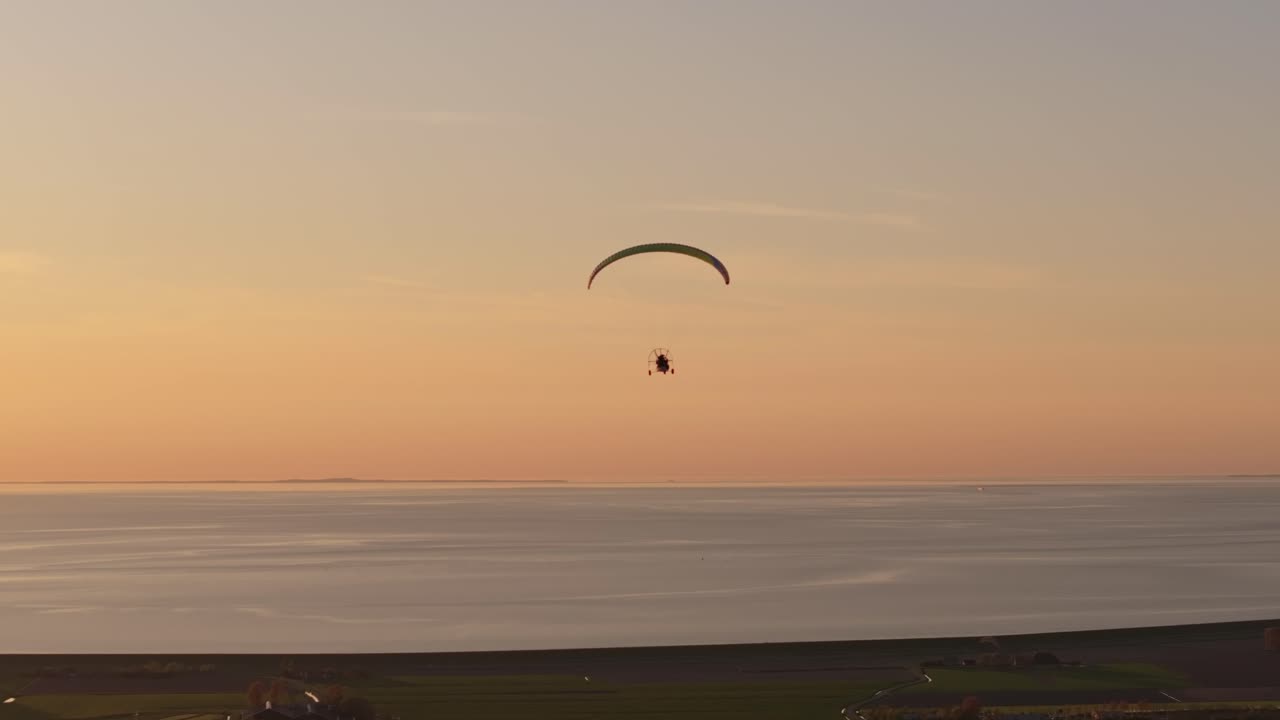 Aerial view of powered paraglider soaring above fields in Dutch twilight