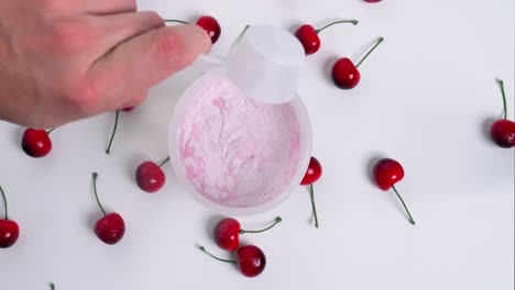 Birdseye-slow-motion-shot-from-a-shaker-filled-with-water-while-a-scoop-of-finest-cherry-whey-powder-is-added-for-a-delicious-cherry-drink-for-sports-with-surrounding-red-cherries