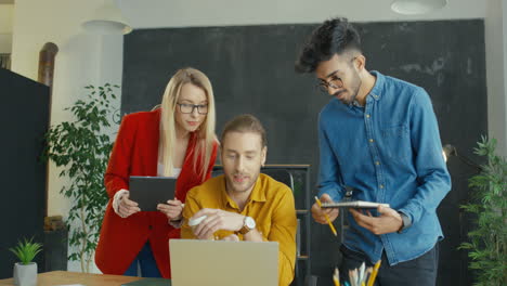 young woman and two men entrepreneurs talking and disputing over business strategy in front of laptop in office