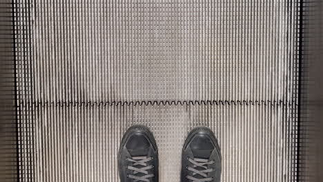 male feet in black sneakers on escalator in shopping mall, top view pov