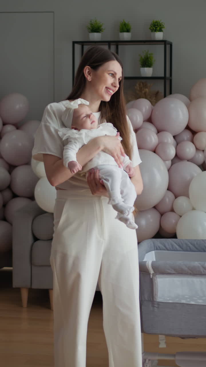 Joven madre acuna tiernamente a su hija pequeña, rodeada de suaves globos pastel, creando un