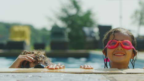 portrait of two children wearing swimming goggles looking over edge of outdoor pool on vacation