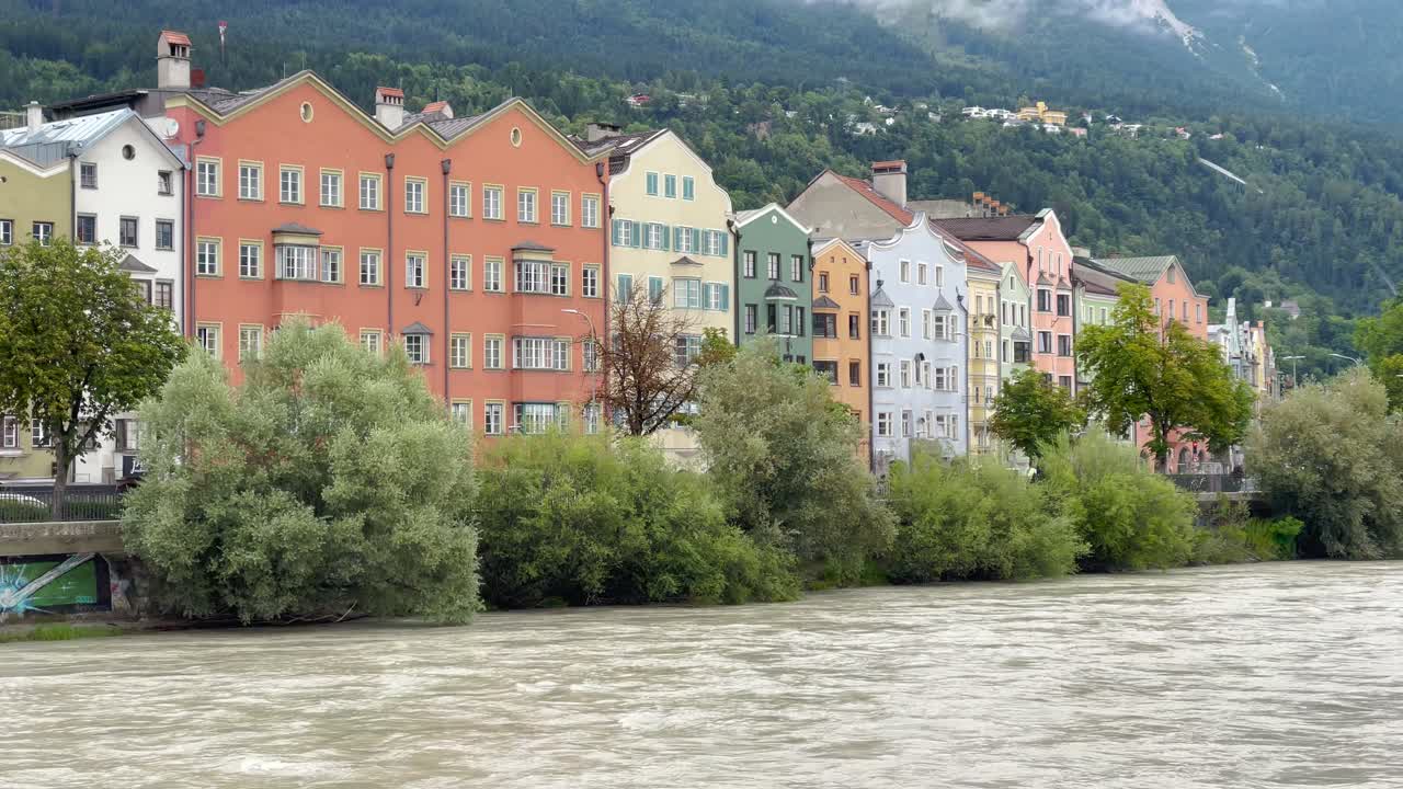 Ripresa statica in una giornata nuvolosa che mostra gli iconici edifici colorati lungo il fiume Inn a Innsbruck con le Alpi della Nordkette avvolte nella nebbia sullo sfondo.