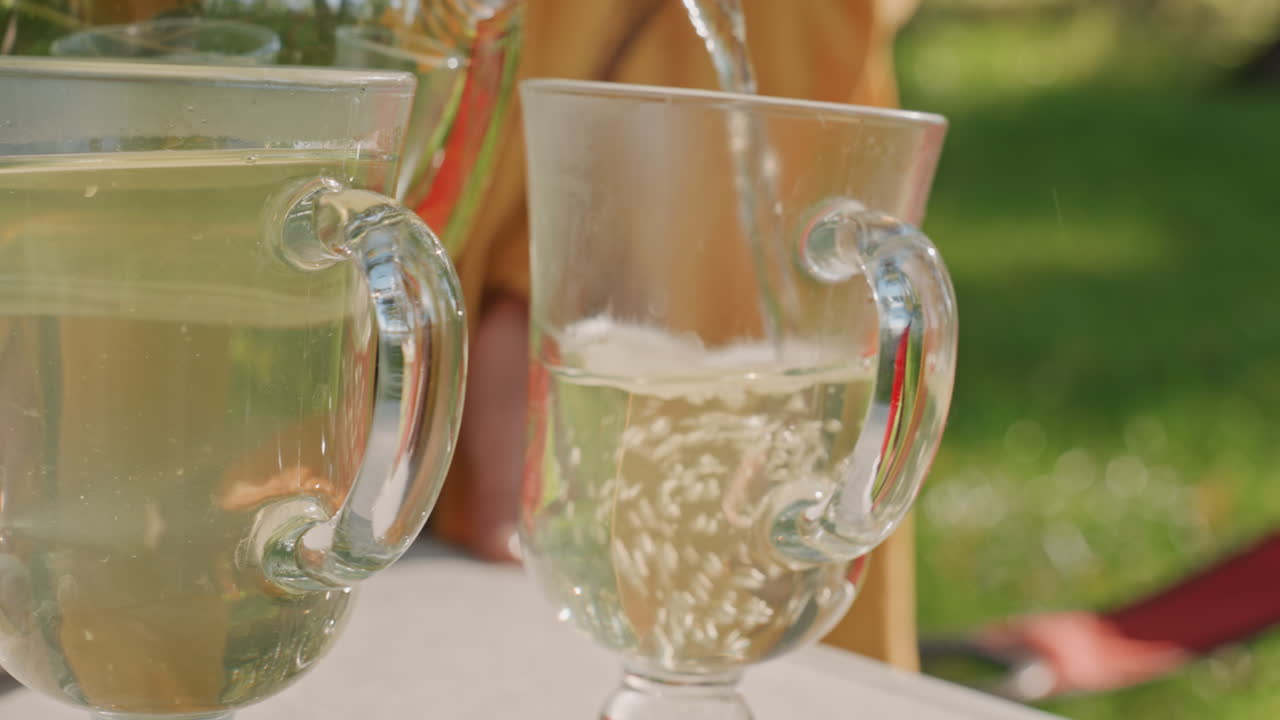 Bevanda frizzante versata in un bicchiere di cristallo, primo piano di un tavolo da campeggio con bollicine e condensa, sfondo esterno luminoso e delicati riflessi del bicchiere, un dettaglio rinfrescante di picnic.