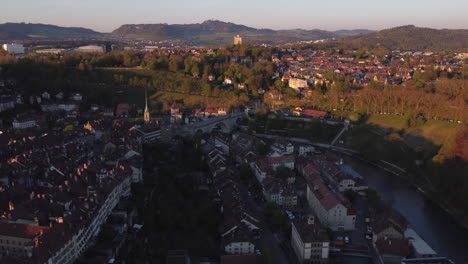 Slow-aerial-shot-high-above-Bern,-Switzerland-with-vehicles-crossing-a-large-stone-bridge-at-sunset