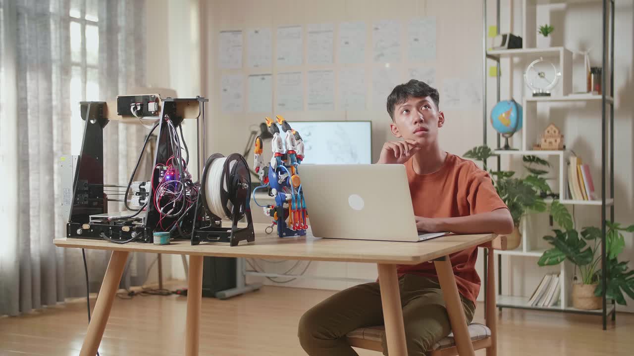 아시아 소년은 집에서 노트북에서 사이보그 손에 대해 작업하는 동안 지표손가락을 생각하고 올립니다.