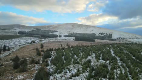 Paisaje-Montañoso-Nevado-Con-Bosques-De-Coníferas-Y-Caminos-Despejados,-Bajo-Un-Cielo-Parcialmente-Nublado,-Vista-Aérea