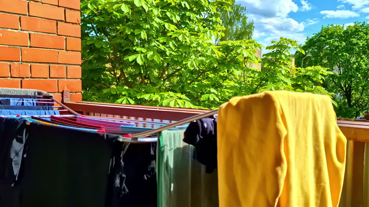 Colourful clothing laundry hanging on maiden to dry on outdoor balcony in bright sunlight