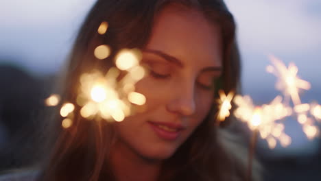 close up sparklers portrait of attractive caucasian woman celebrating new years eve enjoying independence day celebration on beach at sunset