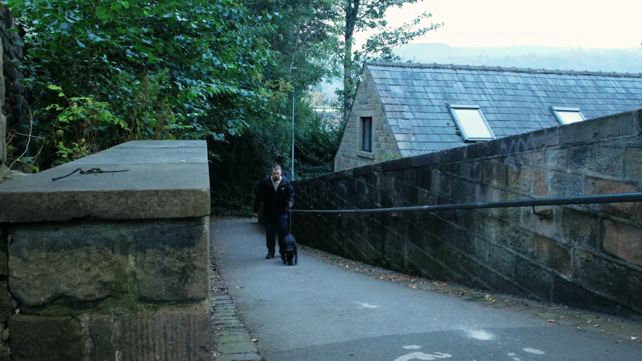 A man walks his black dog up a path first thing in a morning before sunlight