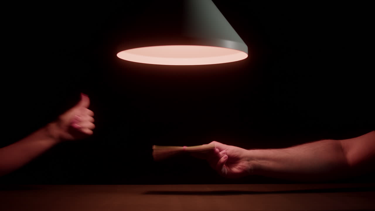 Hände tauschen einen Geldstapel unter einer gedämpften Lampe im Dunkeln.