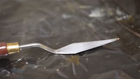 pan across silver palette knife with gold wooden handle on black rubber background