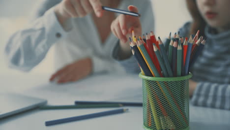 colored pencils close-up. young woman helps little girl to do homework.