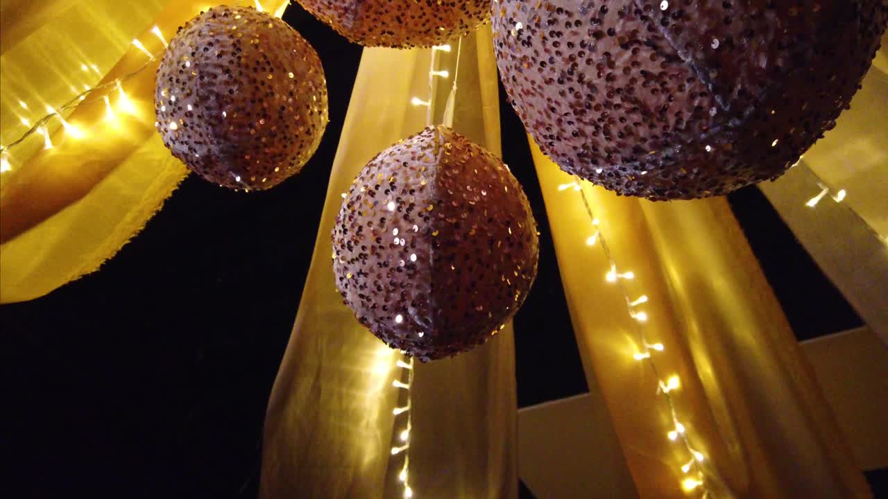 Camera shot of handmade suspended spheres with reflective decorations, surrounded by string lights and golden fabrics inside an exhibition hall in Mexico City