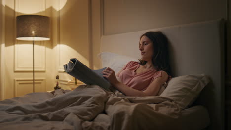 evening woman reading novel in cozy bed. smiling relaxed reader resting home