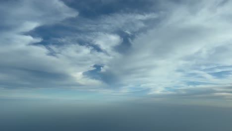 Cockpit-view-from-a-jet-flying-bellow-some-white-few-clouds-with-a-deep-blue-sky,-daylight