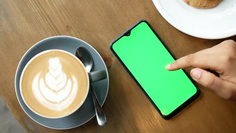 smartphone with green screen at cafe table with latte