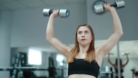 pretty woman in black top raises up dumbbells on the background of the gym. exercises for biceps. close-up