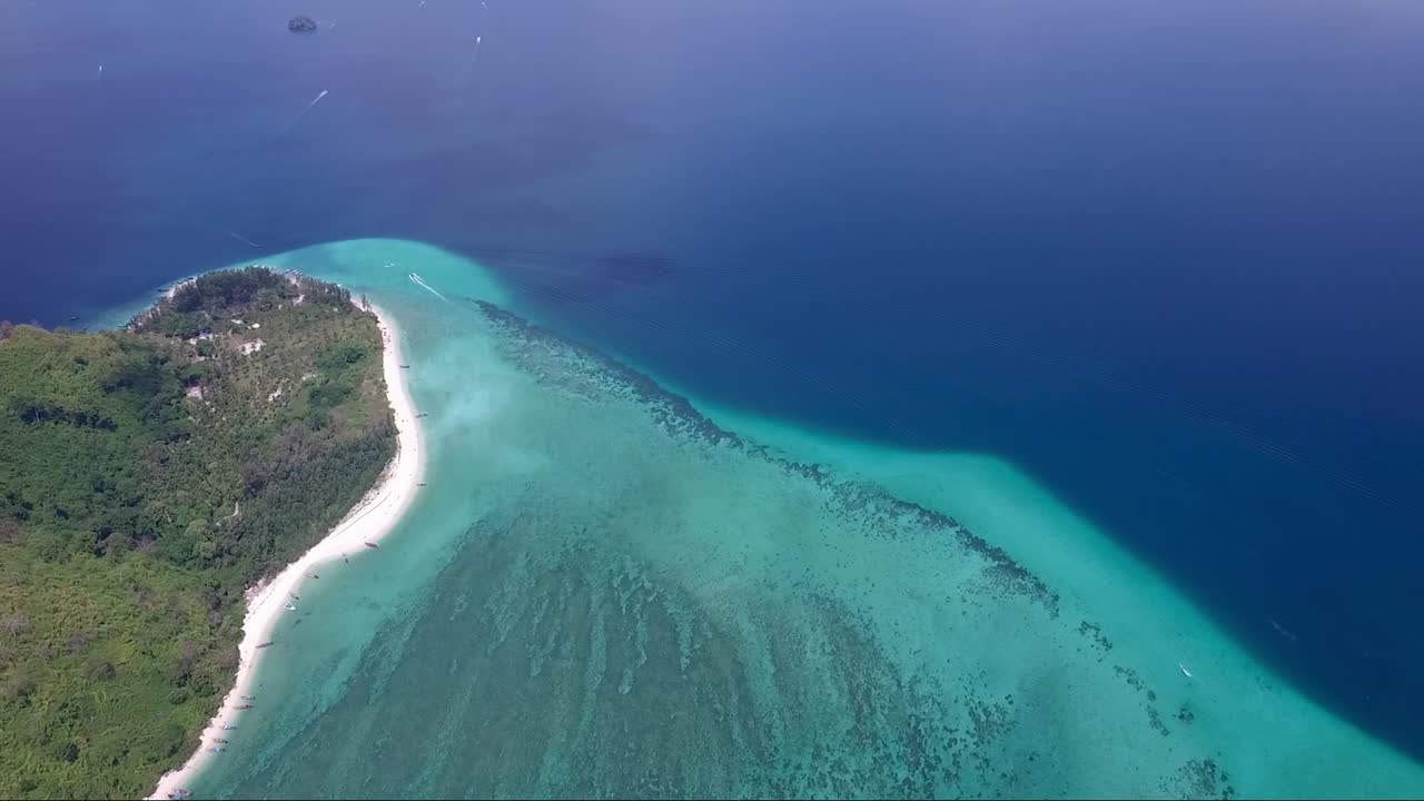 toma aérea panorámica desde agua turquesa y azul marino hasta una isla tropical montañosa