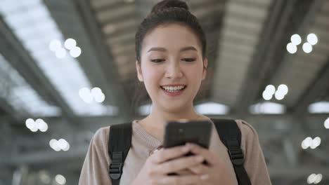 happiness traveller asian female woman wear casual cloth and backpack hand use smartphone chat with friend walking along in airport terminal travel after covid lockdown is over travel concept