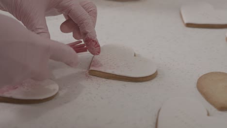 un primer plano de una mujer rociando galletas de mantequilla en forma de corazón con colorante alimentario saludable, 4k