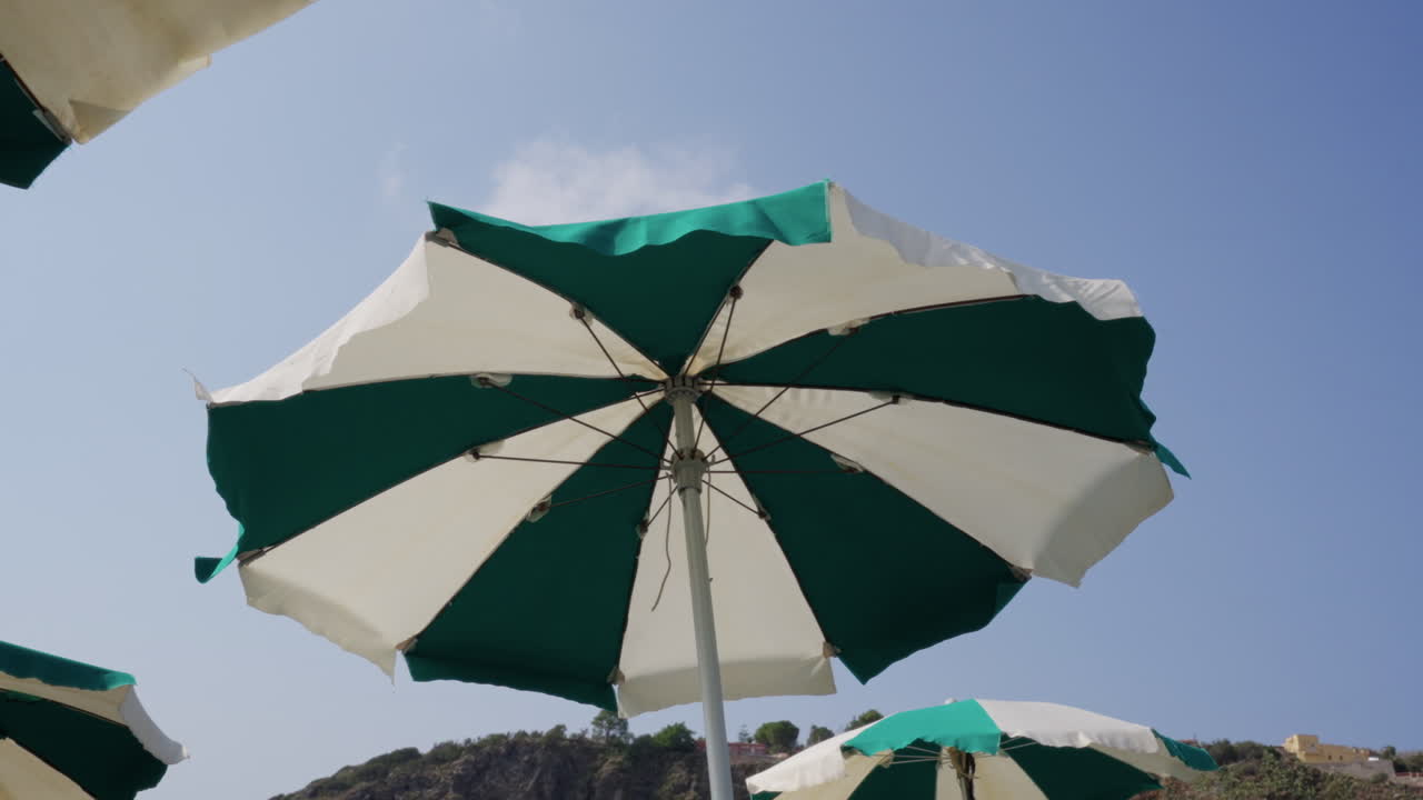 Ombrelloni da spiaggia in Sicilia che ondeggiano al vento sotto il cielo azzurro vicino al Mar Mediterraneo, viaggio estivo, relax al mare e clima caldo