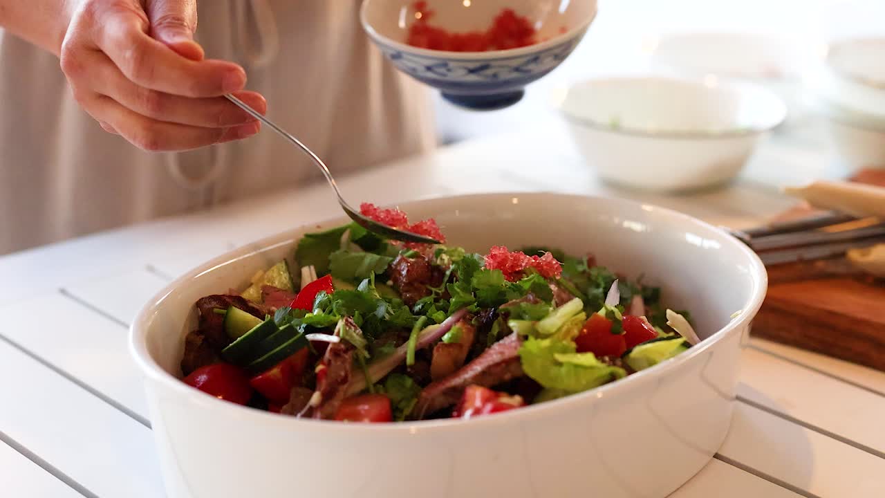 Hands adding ingredients to a colorful beef salad in a well-lit kitchen setting, emphasizing freshness and vibrant colors